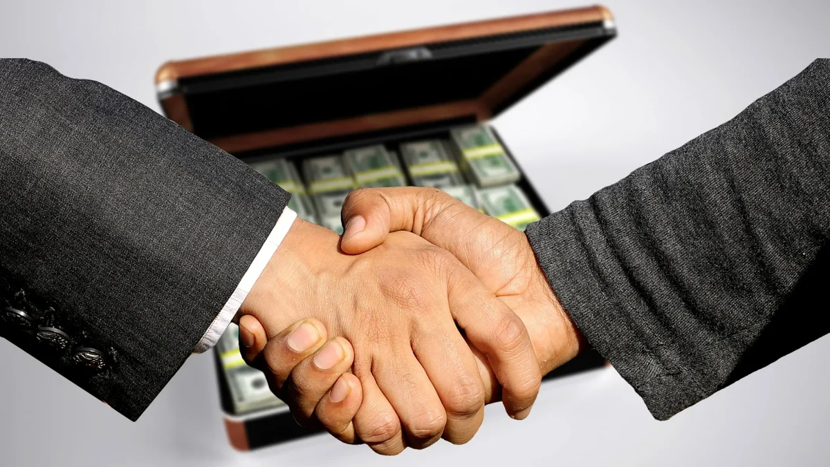 Two people shaking hands over an open briefcase full of cash