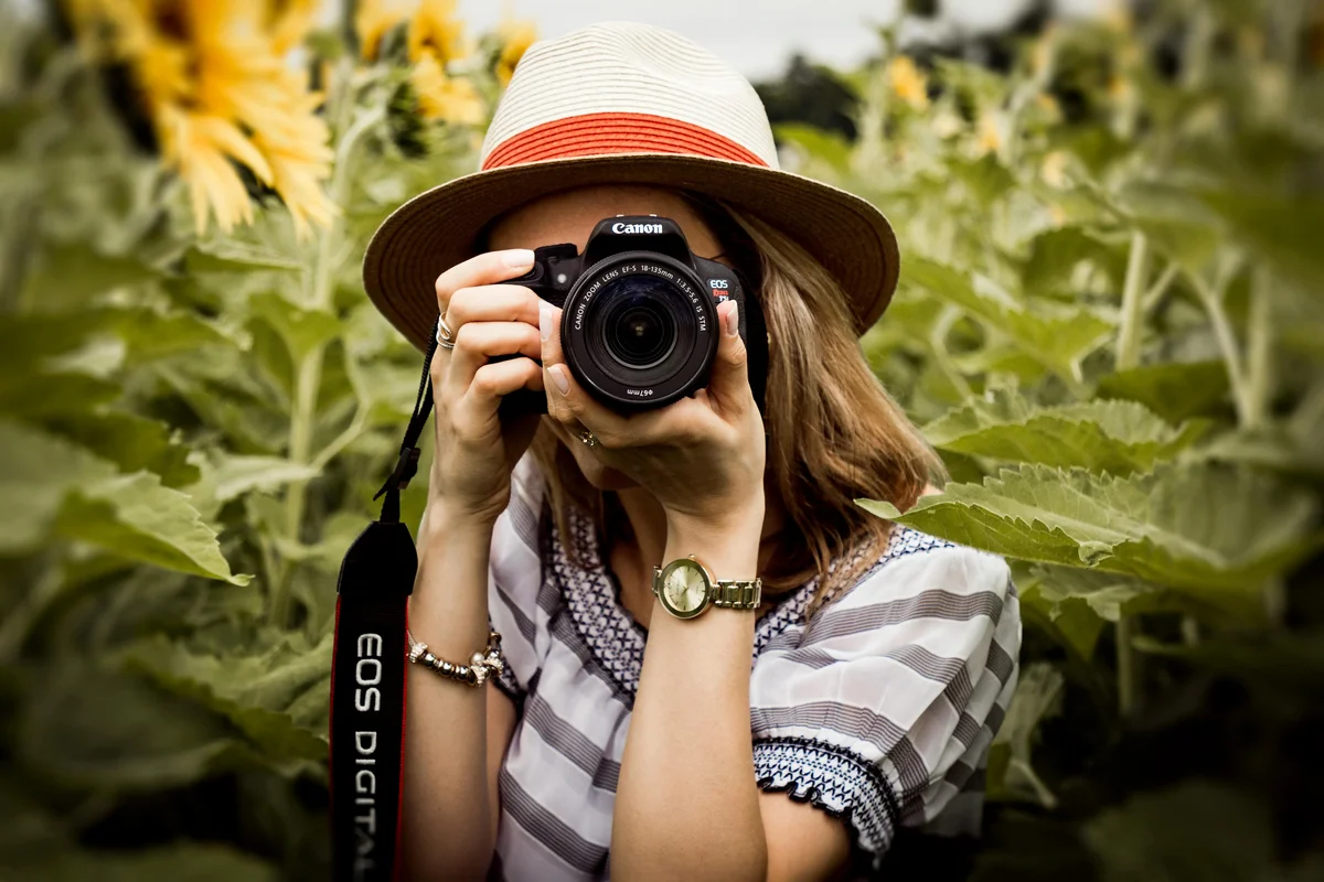 Woman in a sun hat aiming a Canon camera in a sunflower field