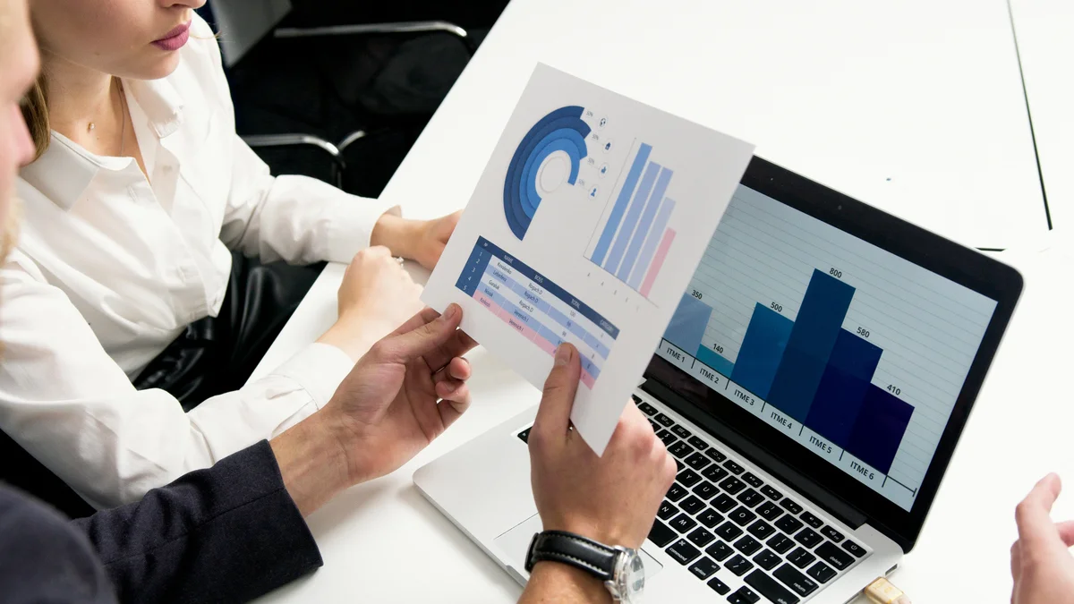 Two people reviewing a printed bar chart in front of a laptop