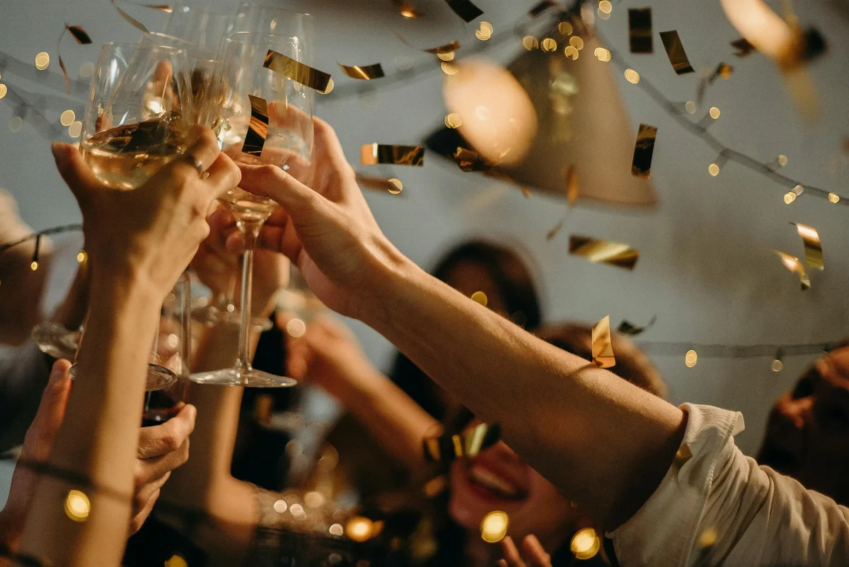 Hands raising glasses in a toast amid falling golden confetti