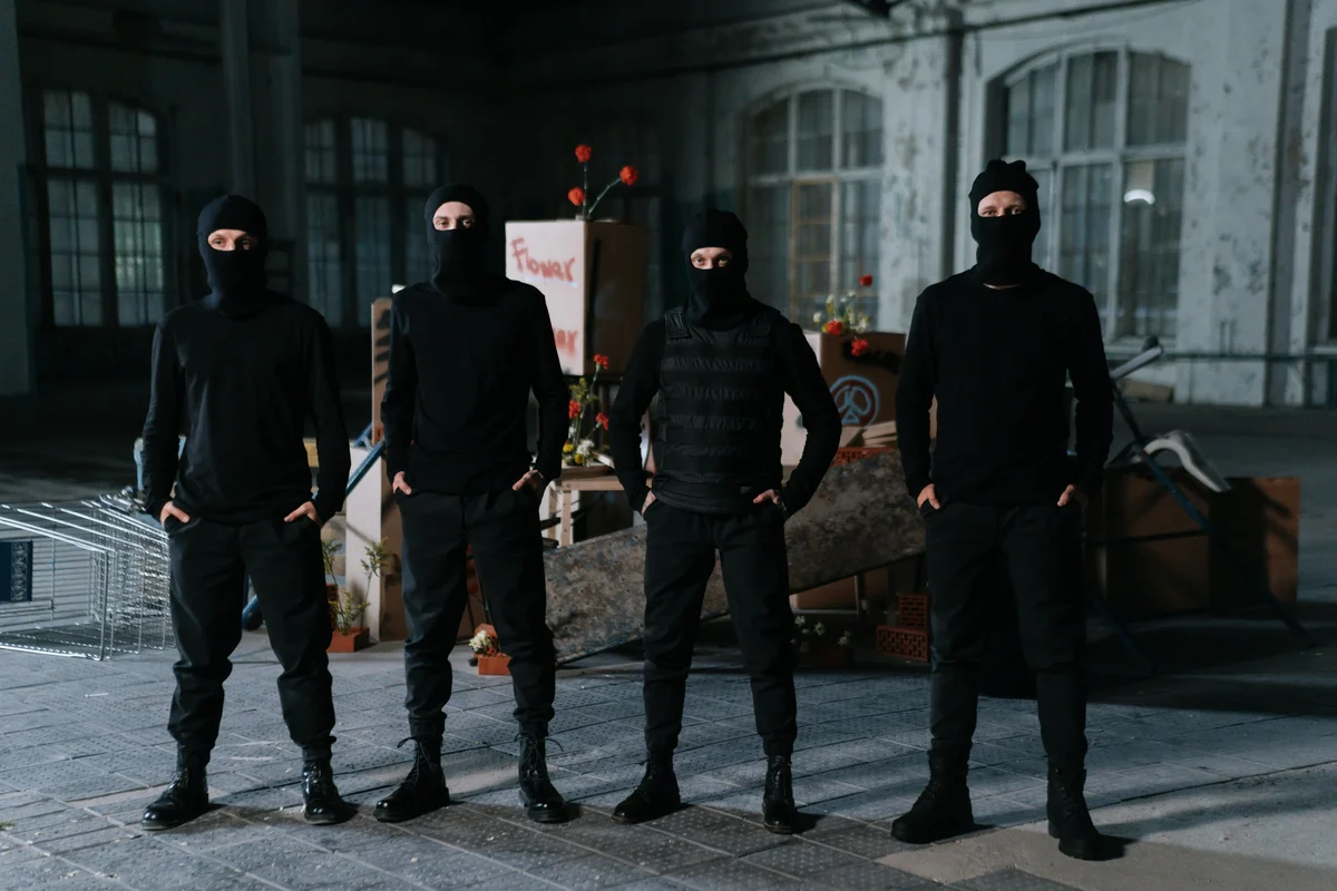 Four people in black balaclavas standing in a row in a derelict building