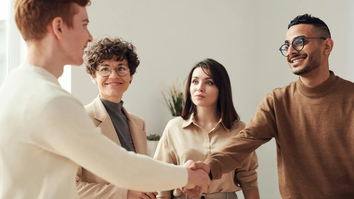 Four people in business casual smiling and shaking hands in an office