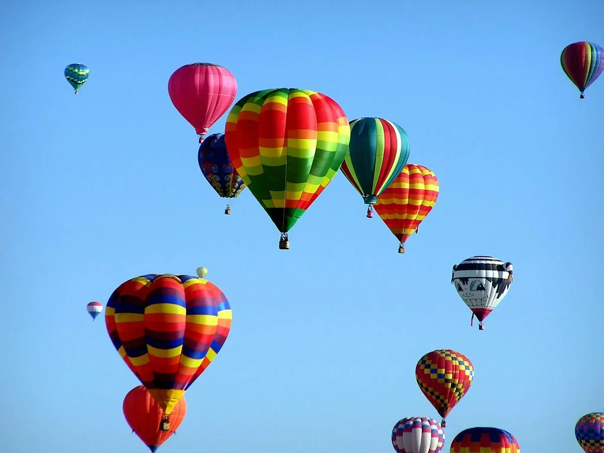 Many colorful hot air balloons rising together against a clear blue sky