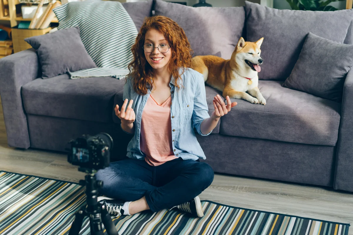 Woman filming herself with a tripod camera, a Shiba Inu on the couch behind her