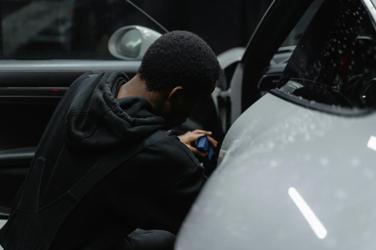 Person in a black hoodie polishing the front fender of a grey car