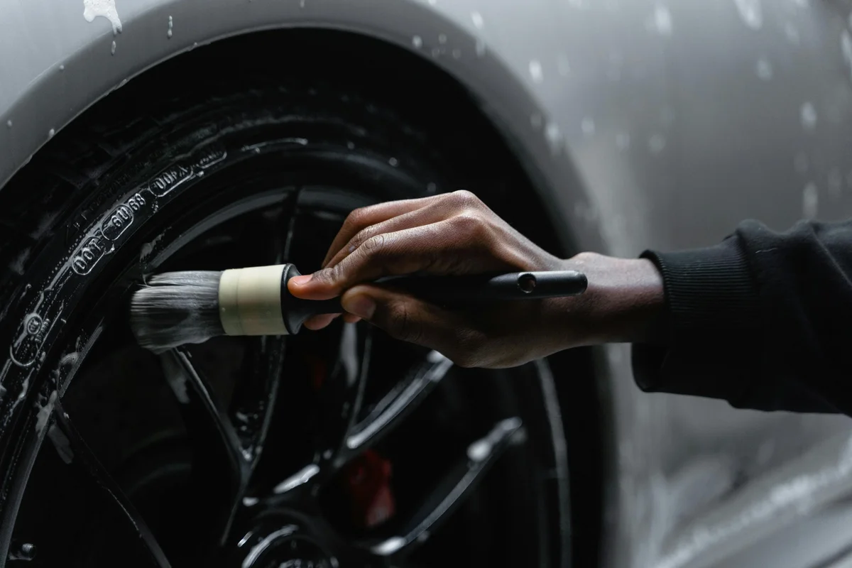 Hand using a detailing brush to clean a black car wheel