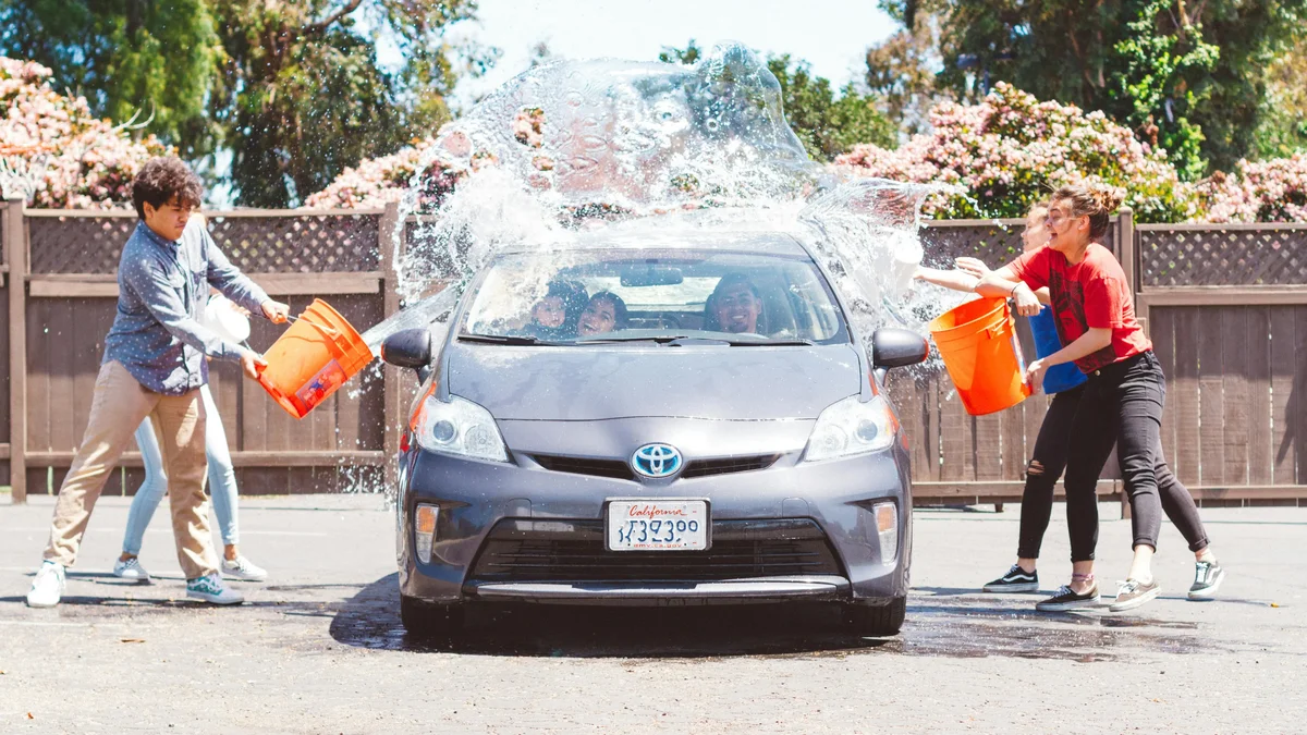 Young people splashing buckets of water while washing a car outdoors