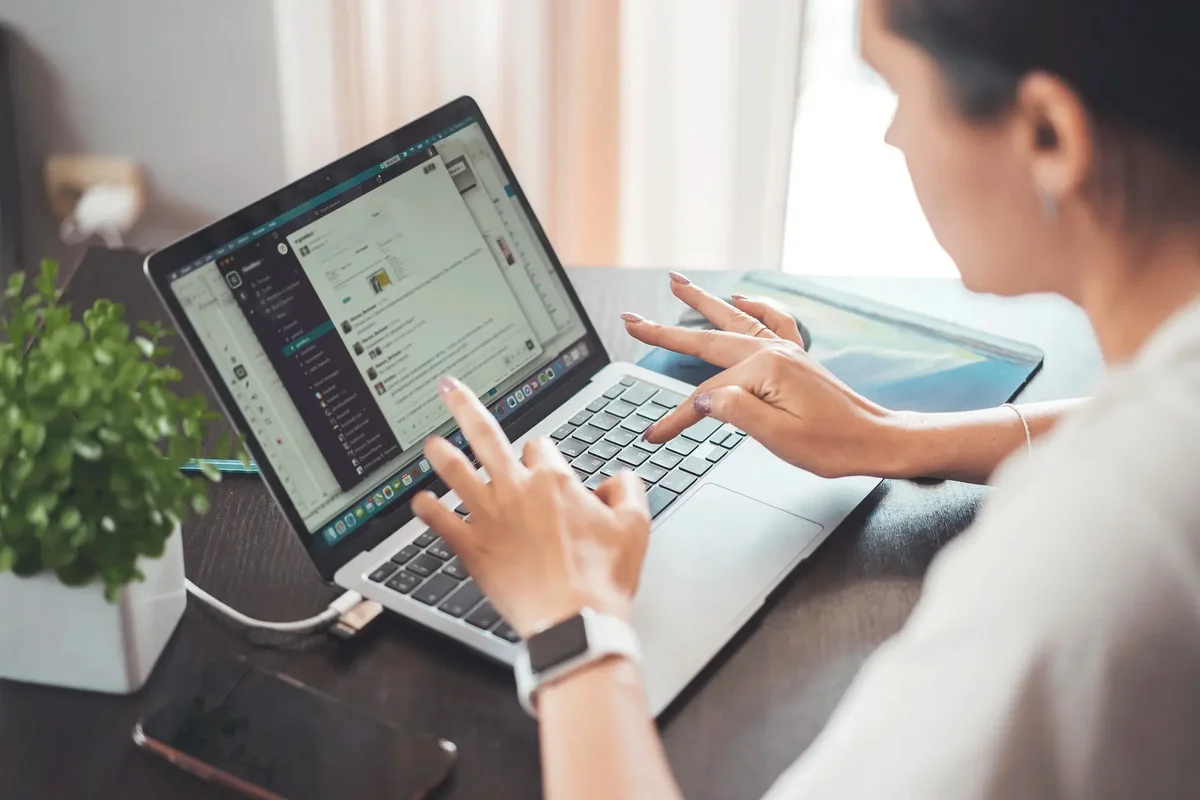 Woman using a chat app on a laptop at a desk beside a potted plant
